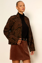 Load image into Gallery viewer, A woman modeling a brown paisley patterned jacket over a black turtleneck and a brown mini skirt, standing against a plain off-white background.
