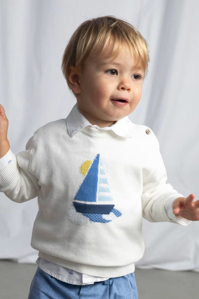 Child wearing a white sweater with a sailboat design on a plain background