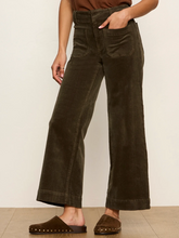 Load image into Gallery viewer, A woman wearing dark olive brown wide-leg corduroy pants with a high waist, front patch pockets, and cuffed hems, paired with brown suede mule slide sandals.
